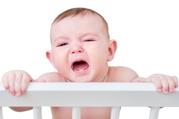 A sad baby is crying in a crib, holding onto the handrails, isolated on a white background. Funny child in bed, age six months