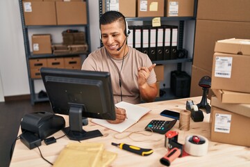 Hispanic young man working at small business ecommerce smiling happy pointing with hand and finger to the side