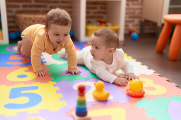 Two toddlers playing with toys sitting on floor at kindergarten