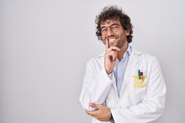 Hispanic young man wearing doctor uniform looking confident at the camera smiling with crossed arms and hand raised on chin. thinking positive.