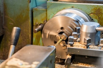 A turner drills a threaded hole in a bronze hexagon on a lathe.