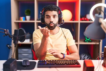 Hispanic man with beard playing video games with headphones looking at the camera blowing a kiss with hand on air being lovely and sexy. love expression.