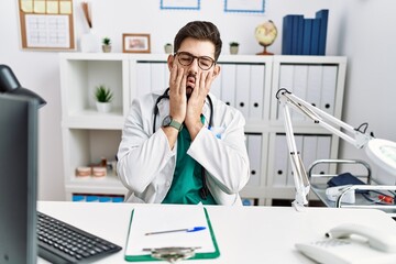 Young man with beard wearing doctor uniform and stethoscope at the clinic tired hands covering face, depression and sadness, upset and irritated for problem