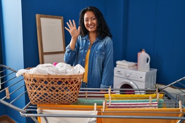 Young asian woman hanging clothes at clothesline showing and pointing up with fingers number five while smiling confident and happy.