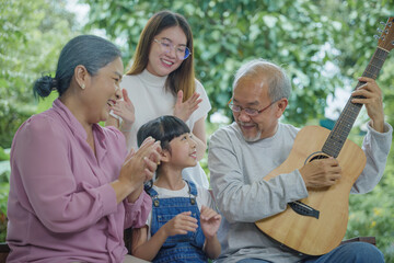 Happy family Asian senior elderly man or grandfather playing guitar while his grandmother and...