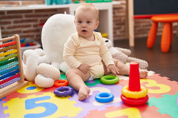 Obraz premium Adorable caucasian baby playing with hoops toy sitting on floor at kindergarten