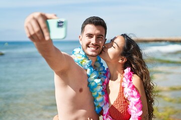 Young hispanic couple tourists wearing hawaiian lei make selfie by smartphone at seaside