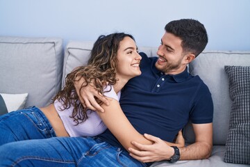 Young hispanic couple hugging each other lying on sofa at home