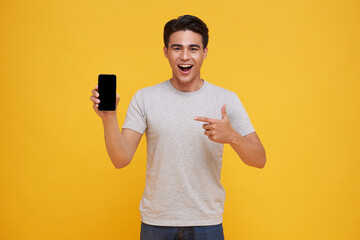 Happy young Asian man showing and pointing at blank screen smartphone great mobile offer isolated...