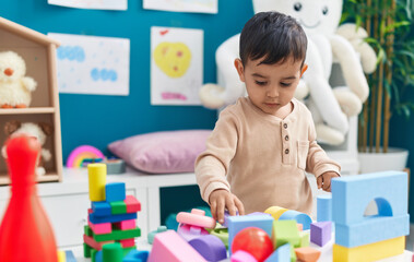 Adorable hispanic toddler playing with construction blocks standing at home