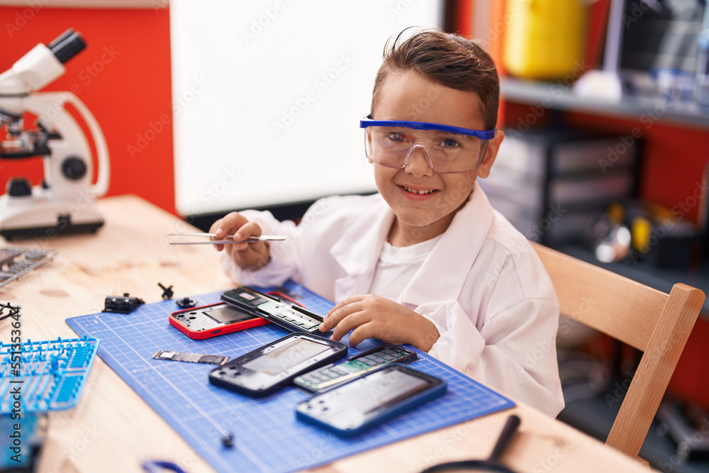 Poster Adorable hispanic toddler student repairing smartphone at classroom