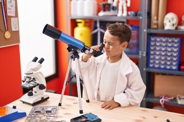 Adorable hispanic toddler student using telescope at classroom