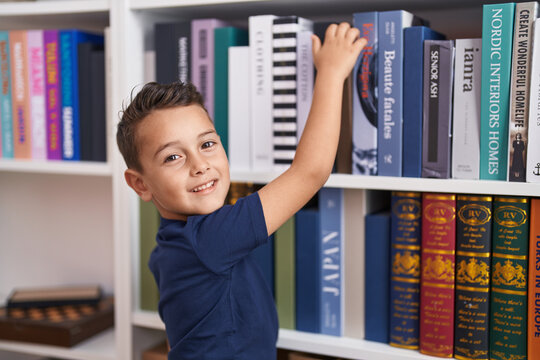 Adorable hispanic toddler smiling confident holding book of shelving at library school
