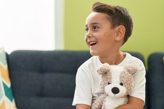 Adorable hispanic toddler hugging teddy bear sitting on sofa at home