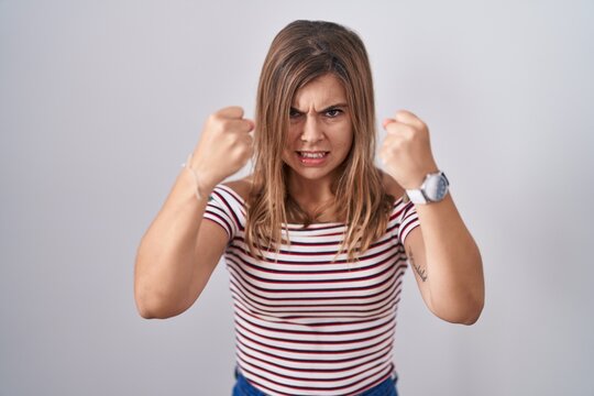 Young hispanic woman standing over isolated background angry and mad raising fists frustrated and furious while shouting with anger. rage and aggressive concept.