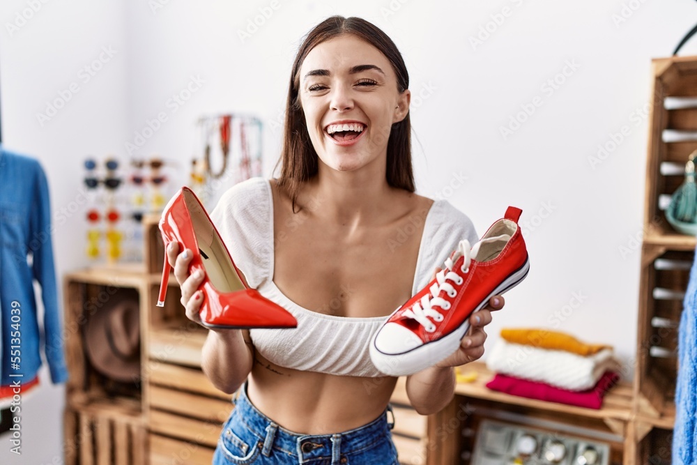 Poster young hispanic customer woman holding high heel shoes and sneaker smiling and laughing hard out loud