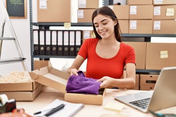 Young hispanic woman smiling confident packing clothes box at warehouse