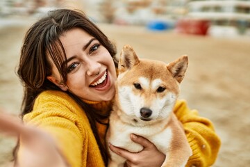 Beautiful young woman hugging happy shiba inu dog at the beach