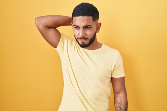 Young hispanic man standing over yellow background confuse and wondering about question. uncertain with doubt, thinking with hand on head. pensive concept.