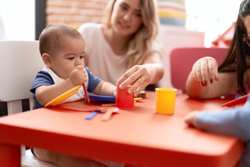 Obraz na płótnie Canvas Teacher and preschool student learning to eat sitting on table at kindergarten