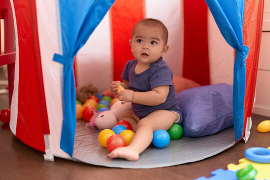 Adorable chinese toddler playing with balls sitting inside of circus tent at home