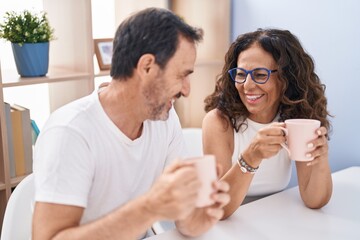 Man and woman couple drinking coffee sitting on table at home