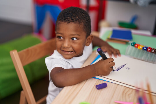 African american boy preschool student sitting on table drawing on notebook at kindergarten