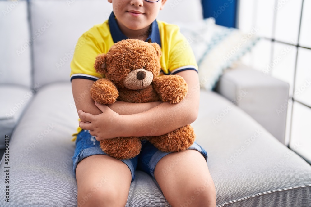 Sticker adorable hispanic boy hugging teddy bear sitting on sofa at home