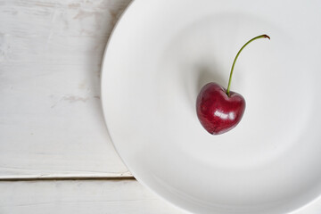 One heart-shaped cherry on a white plate. Ripe fresh juicy berry on a white background. Fruit...