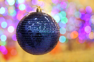 Christmas toy, blue shiny ball hanging on blurred festive lights background. New Year decorations