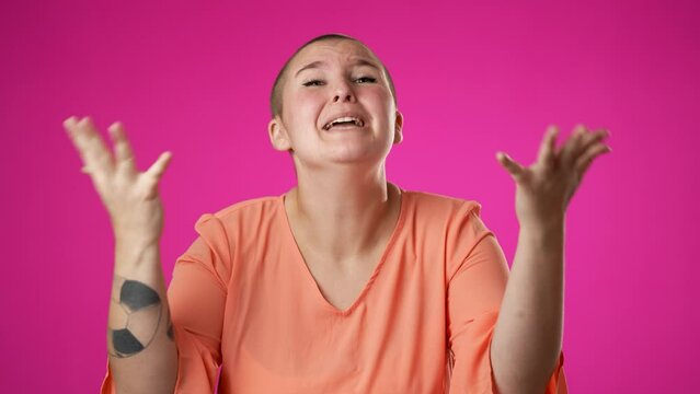Angry, scared young gender fluid non binary woman 20s put hands on head screaming crying ask why me, isolated on pink background studio. Slow motion
