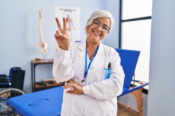 Middle age woman with grey hair working at pain recovery clinic smiling with happy face winking at...