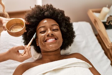 Young african american woman smiling confident having facial treatment at beauty center - Powered by Adobe