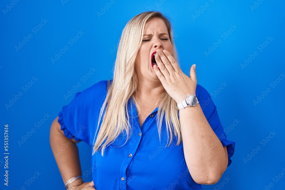 Sticker caucasian plus size woman standing over blue background bored yawning tired covering mouth with hand