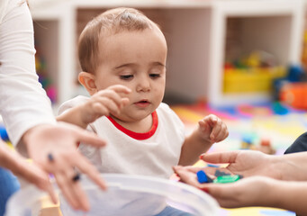 Adorable hispanic baby sitting on floor with relaxed expression at kindergarten