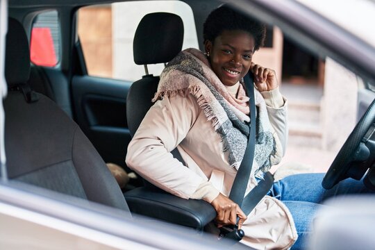African american woman smiling confident fastening seat belt at street