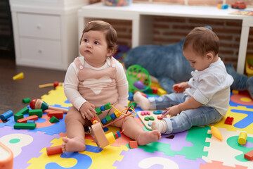 Two toddlers playing with toys sitting on floor at kindergarten