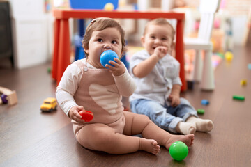 Two toddlers sucking ball sitting on floor at kindergarten