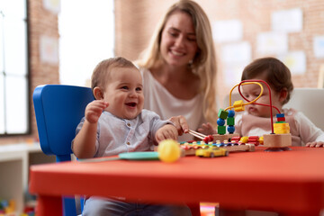 Fototapeta premium Teacher and preschool students playing with toys sitting on table at kindergarten