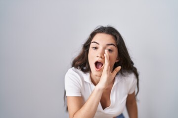 Young teenager girl standing over white background hand on mouth telling secret rumor, whispering...