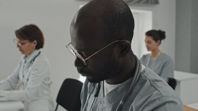 Selective focus close-up of young adult African American general practitioner and his colleagues studying at medical training course