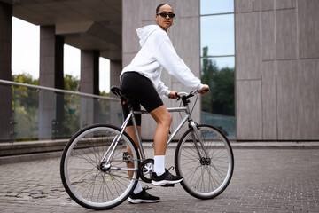 Trendy african american woman in sunglasses standing near bike on street at daytime 