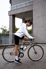 Fototapeta premium Fashionable african american woman in hoodie and sunglasses riding bike on street 