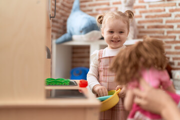 Adorable caucasian girl playing with play kitchen standing at kindergarten