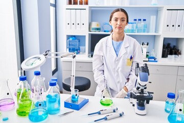 Young brunette woman working at scientist laboratory with serious expression on face. simple and natural looking at the camera.