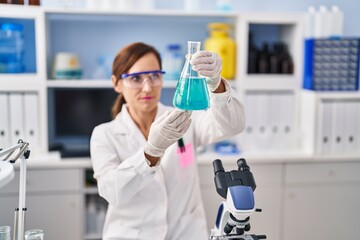 Fototapeta premium Middle age woman wearing scientist uniform measuring liquid at laboratory