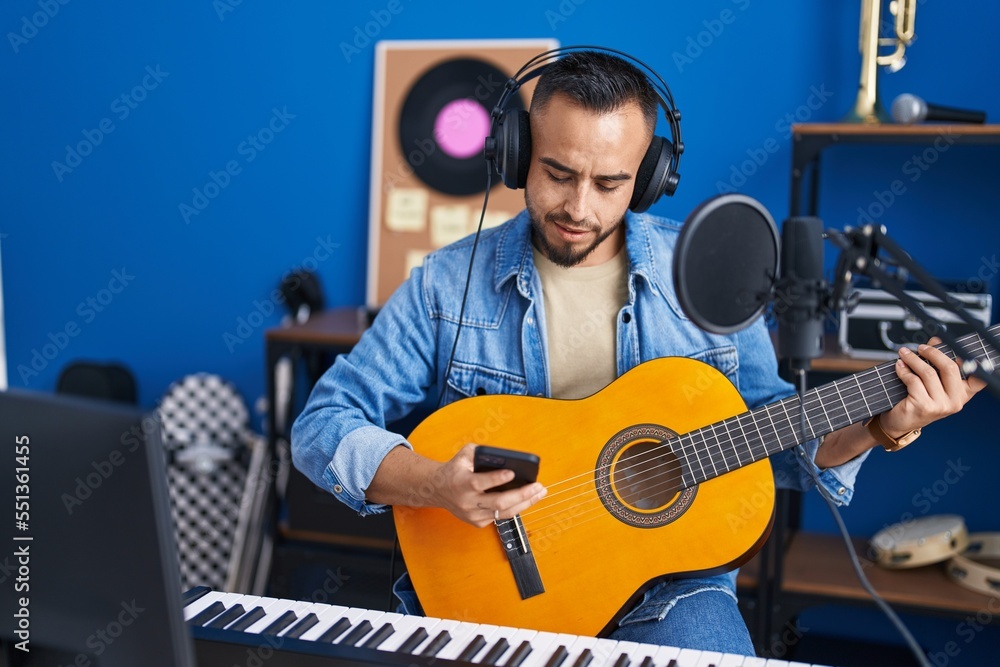 Sticker young hispanic man artist using smartphone playing classical guitar at music studio