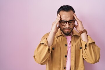 Young hispanic man standing over pink background with hand on head for pain in head because stress. suffering migraine.