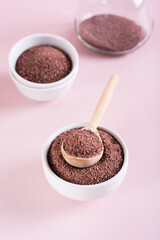 Black Himalayan kala namak salt in bowl with wooden spoon on pink background. Vertical view