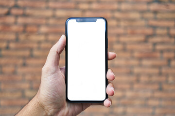 Man holding smartphone showing white blank screen over isolated brick background
